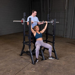 PCL Oly Shoulder Press Bench with user lifting weights under supervision for shoulder workout.