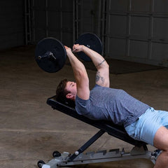 Man performing a bench press exercise with black standard plates, focusing on strength training and muscle building.